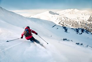 Mężczyzna w czerwonej kurtce jedżący na nartach na stoku we Włoszech 