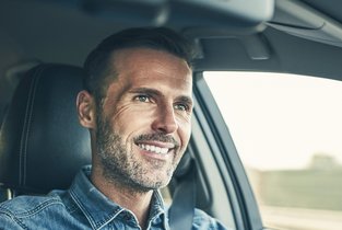 Uśmiechnięty mężczyzna jadący nowym autem, które ma wykupione polisę AC w Warcie 