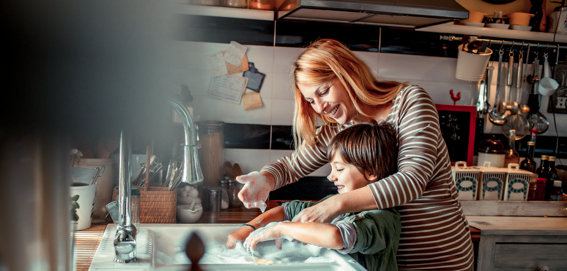 Mama i jej dziecko myją naczynia w kuchni i są ubezpieczeni w Warcie na wypadek ciężkiego zachorowania 