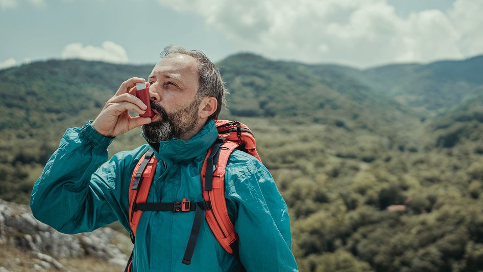Mężczyzna w górach zażywający lek wziewny na astmę, ubezpieczony w Warcie - Warta Travel 