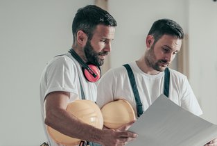 Dwóch mężczyzn w strojach robotniczych w pracy na budowie za granicą, mający wykupione ubezpieczenie turystyczne w Warcie 