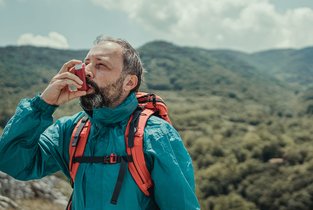 Mężczyzna w górach zażywający lek wziewny na astmę, ubezpieczony w Warcie - Warta Travel 