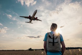 Mężczyzna z plecakiem patrzy na startujący samolot i zastanawia się nad podróżą tanimi liniami lotniczymi.