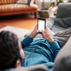 Mężczyzna leży na jasnej kanapie i pisze wiadomość na swoim telefonie ubezpieczonym w Warcie 