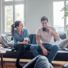 Kobieta z mężczyzną piją kawę na szarej kanapie, którzy oszczędzają na swoją przyszłość z ubezpieczeniem na życie w Warcie 