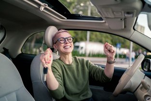Kobieta cieszy się odebranym prawem jazdy po zdanym egzaminie i wsiada pierwszy raz za kółko swojego auta