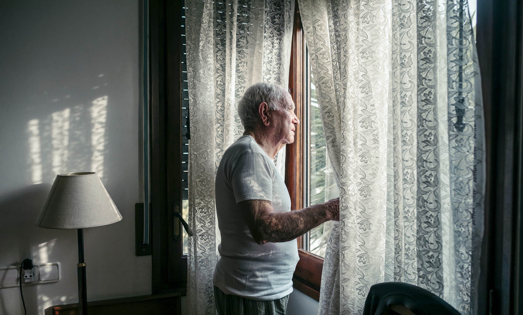 Ubezpieczenie mieszkania - senior w białej koszulce stojący przy oknie Starszy mężczyzna w białej koszulce przy oknie