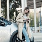 Kobieta w beżowym płaszczu pisząca wiadomość na telefonie jest oparta o srebrny samochód 