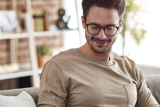 Uśmiechnięty mężczyzna w okularach wypoczywający w swoim mieszkaniu ubezpieczonym w Warcie
