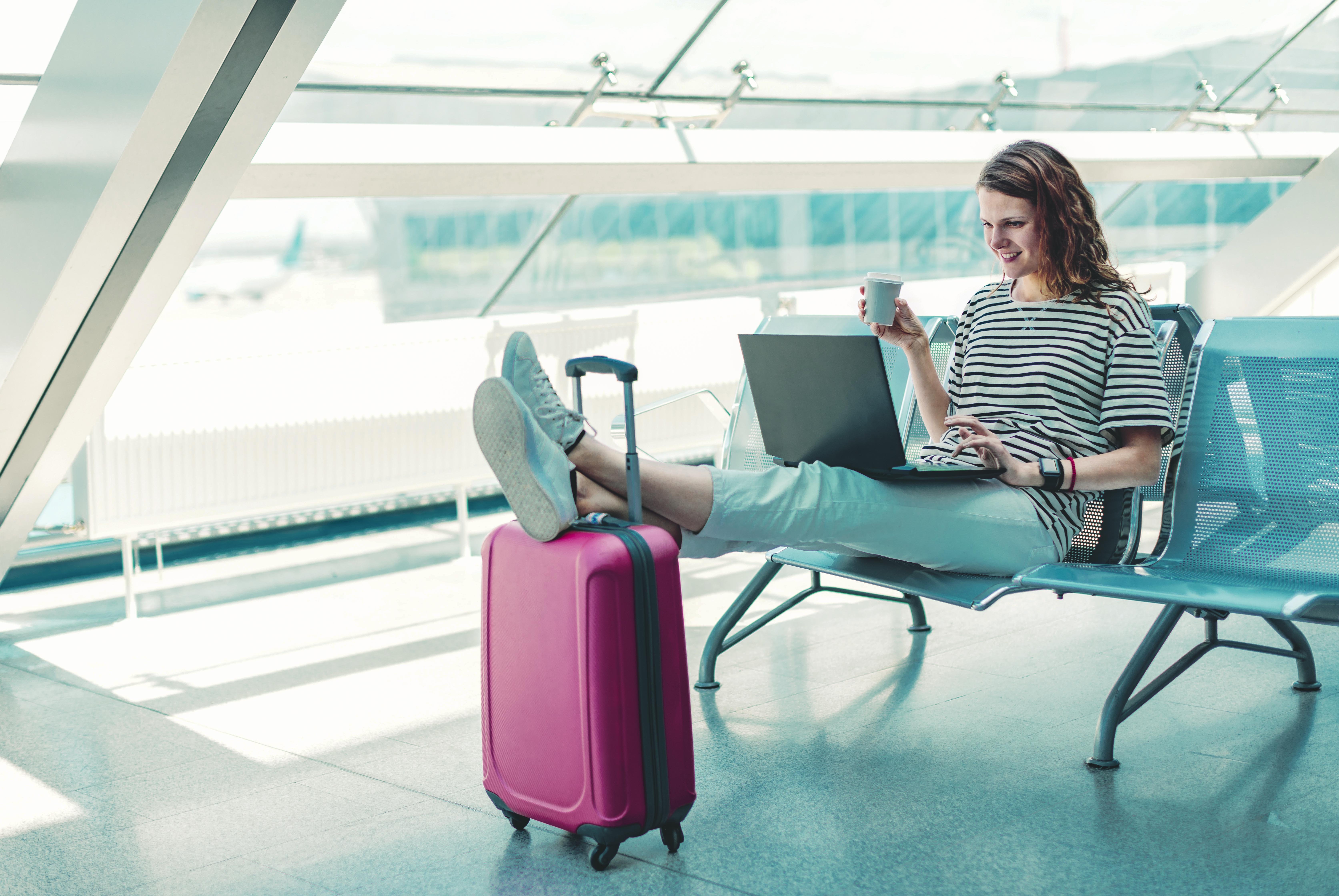 Kobieta czeka na lotnisku z walizką i sprawdza ostatnie informacje przed odprawą, aby wiedzieć, co można zabrać do samolotu.