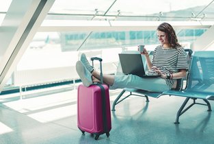 Kobieta czeka na lotnisku z walizką i sprawdza ostatnie informacje przed odprawą, aby wiedzieć, co można zabrać do samolotu.