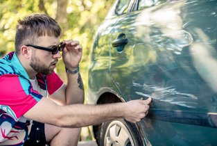 Mężczyznza sprawdza stan swojego pojazdu po obtarciu innego pojazdu na parkingu