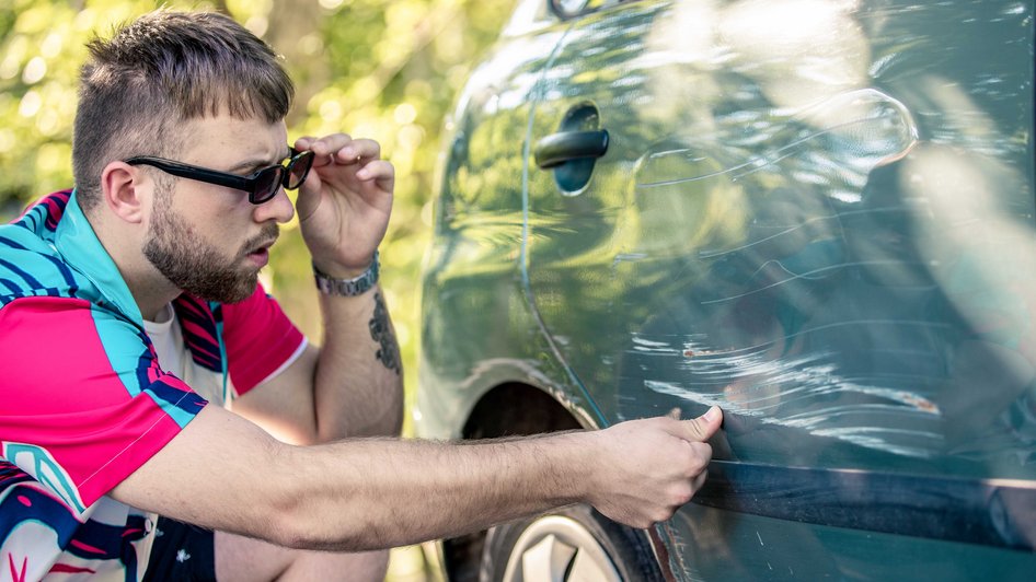 Mężczyznza sprawdza stan swojego pojazdu po obtarciu innego pojazdu na parkingu