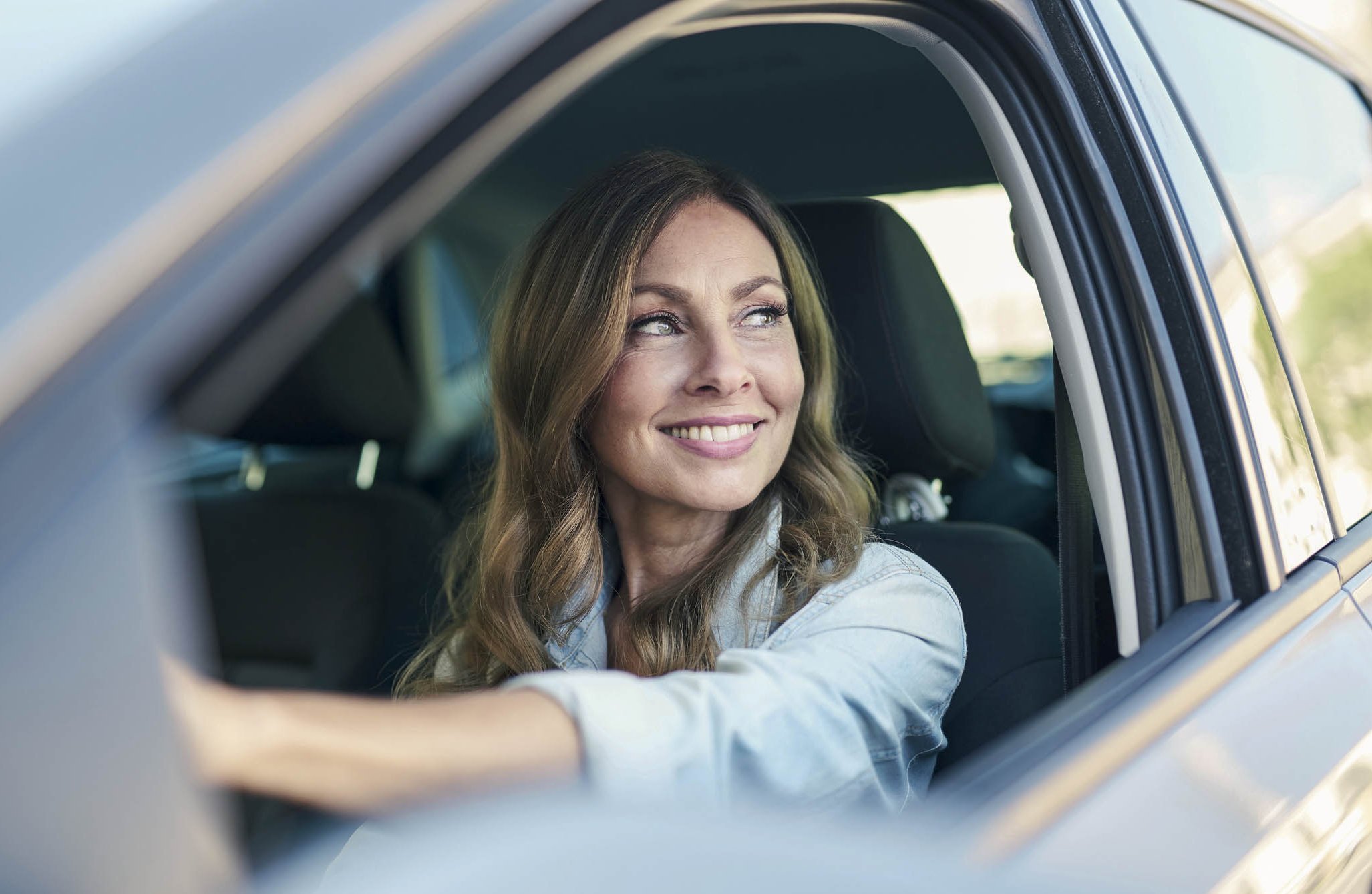 Leasing konsumencki - Uśmiechnięta kobieta w szarym samochodzie ubezpieczonym w Warcie Uśmiechnięta kobieta w szarym samochodzie