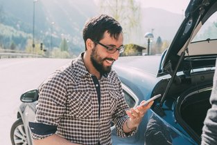 Mężczyzna na tle samochodu przeglądający wiadomości w telefonie