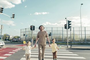 Tata z dwójką dzieci przechodzi przez bezpieczne przejście dla pieszych.