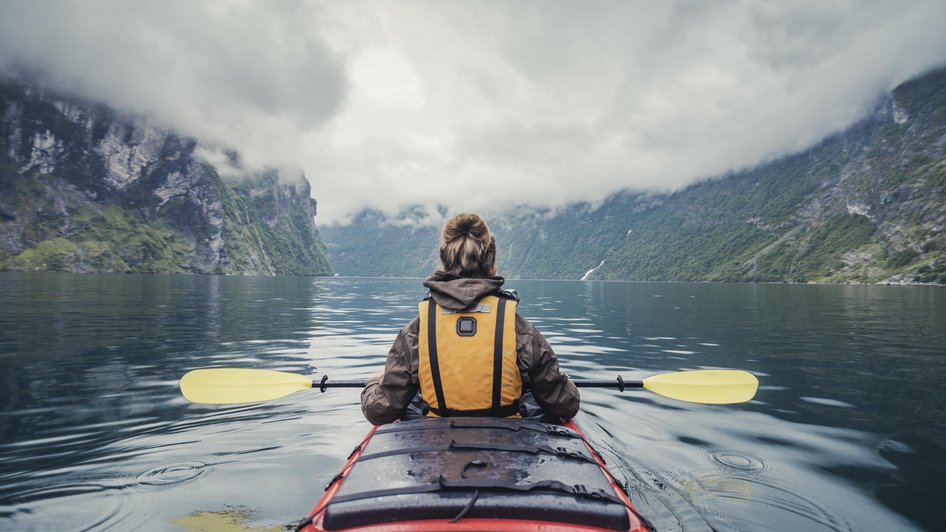Kobieta płynie kajakiem przez skandynawski fjord