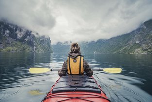 Kobieta płynie kajakiem przez skandynawski fjord