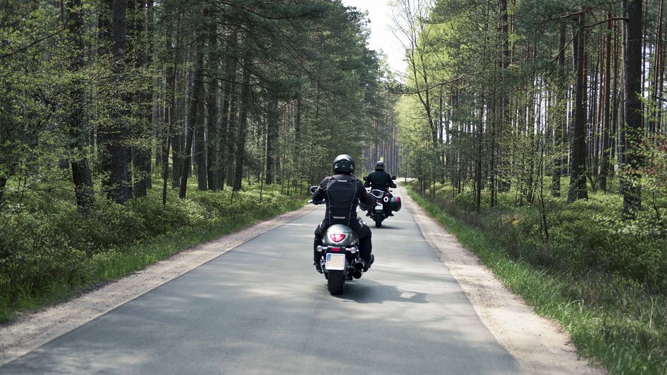 Dwie osoby jadą na motorach przez las i mają zamontowane małe tablice rejestracyjne