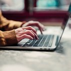 Mężczyzna w żółtej koszuli pisze na laptopie 