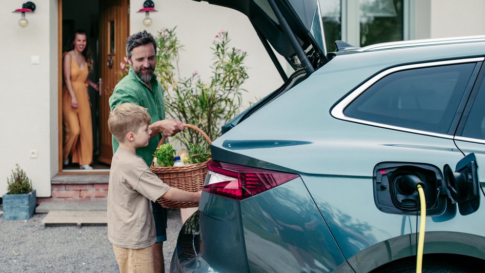 Tata z synem pakują rzeczy do bagażnika w trakcie ładowania hybrydy plug-in
