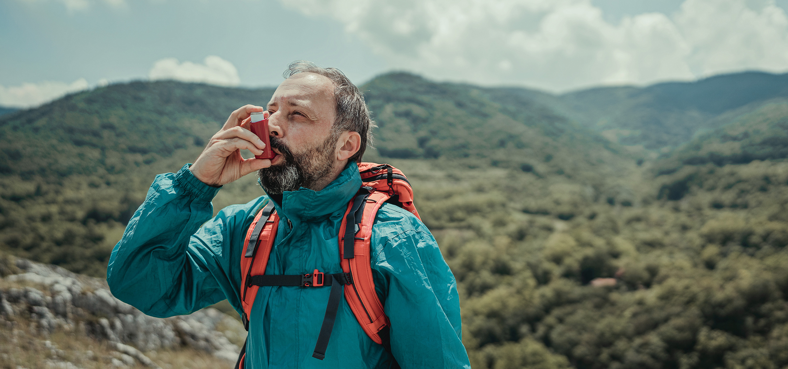 Mężczyzna w górach zażywający lek wziewny na astmę, ubezpieczony w Warcie - Warta Travel 