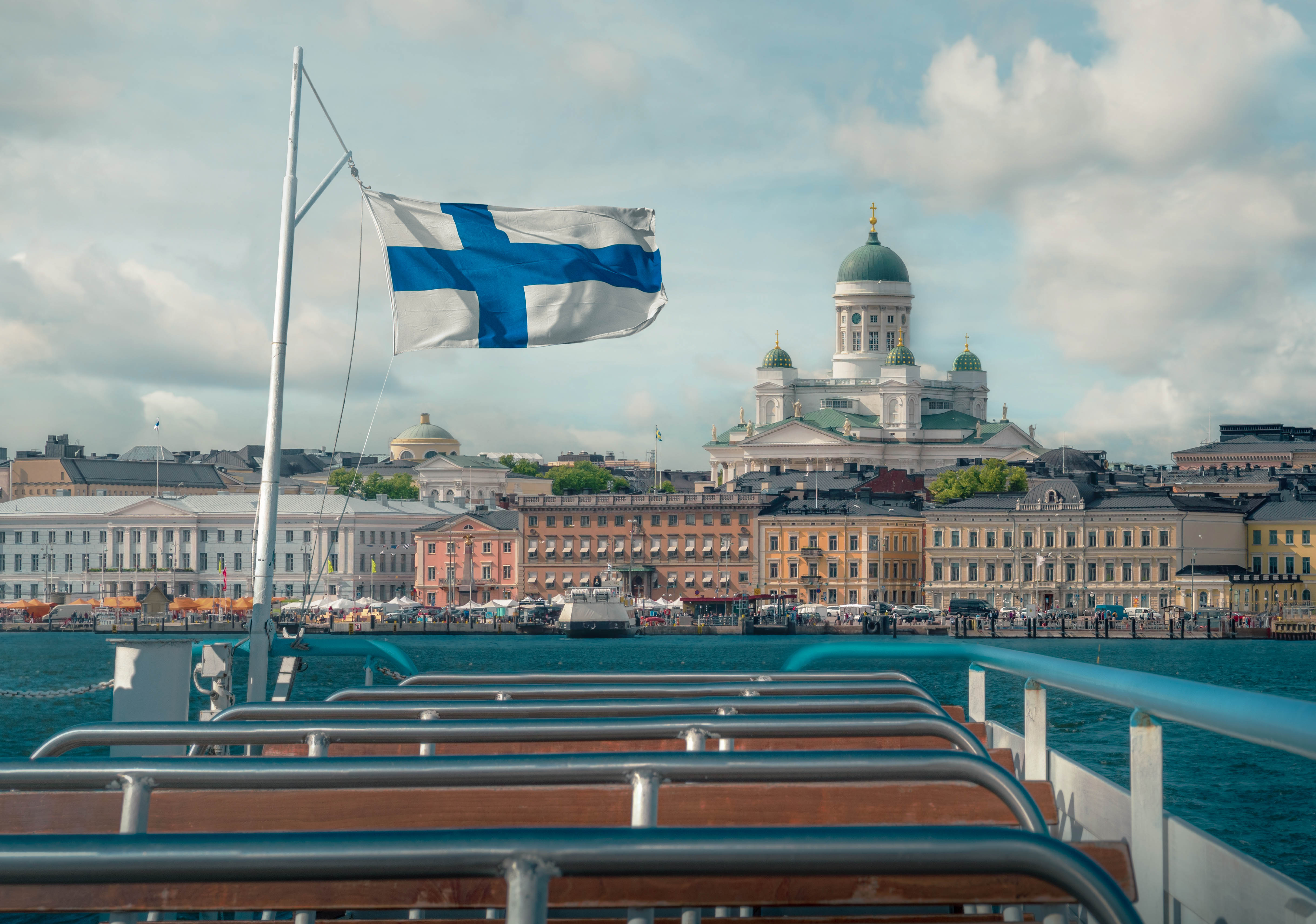 Urlop w Finlandii - ubezpieczenie turystyczne Flaga Finlandii na łódce, a w tle widok na stolicę - Helsinki