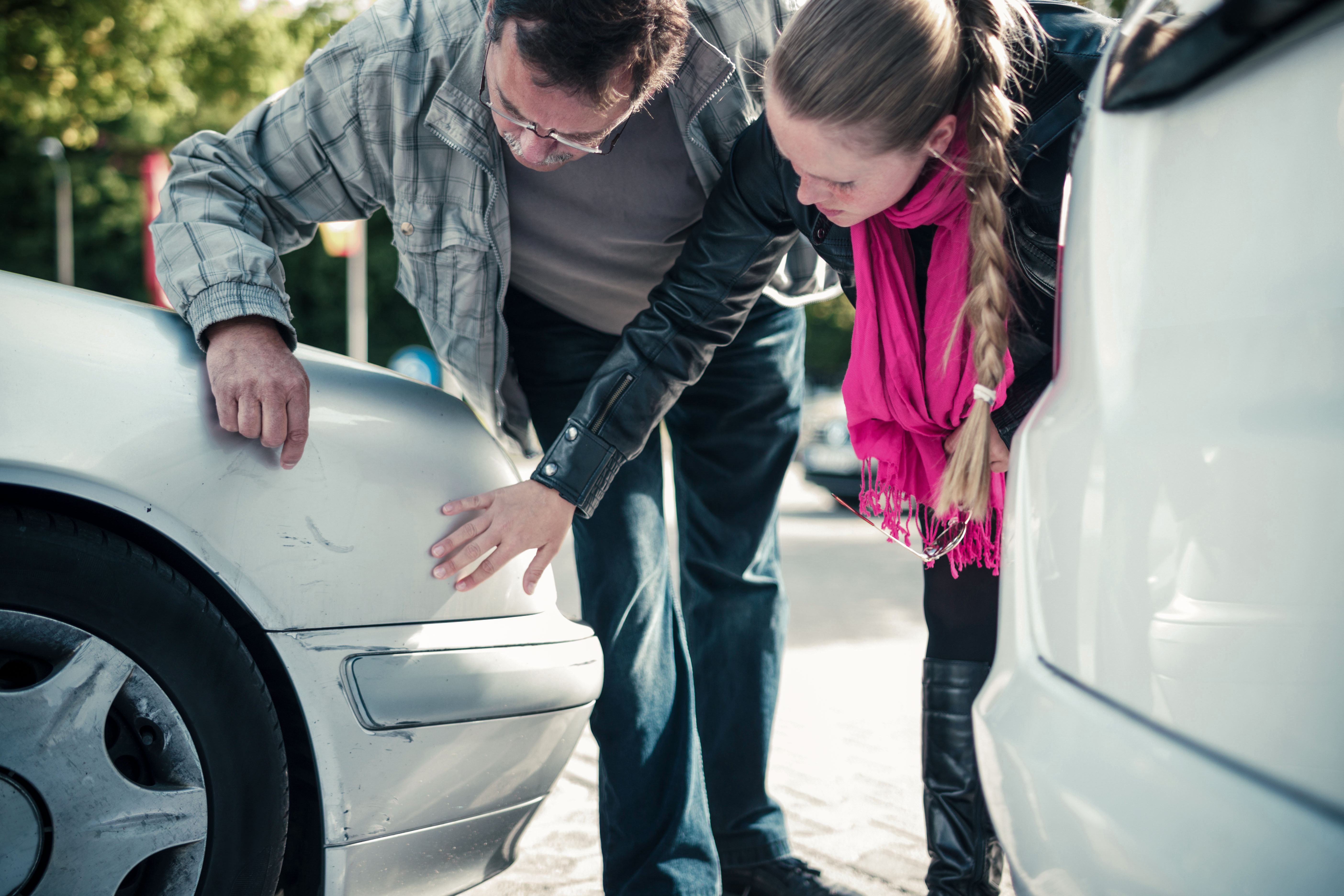 Kobieta i mężczyzna oglądają zarysowania samochodu po stłuczce.