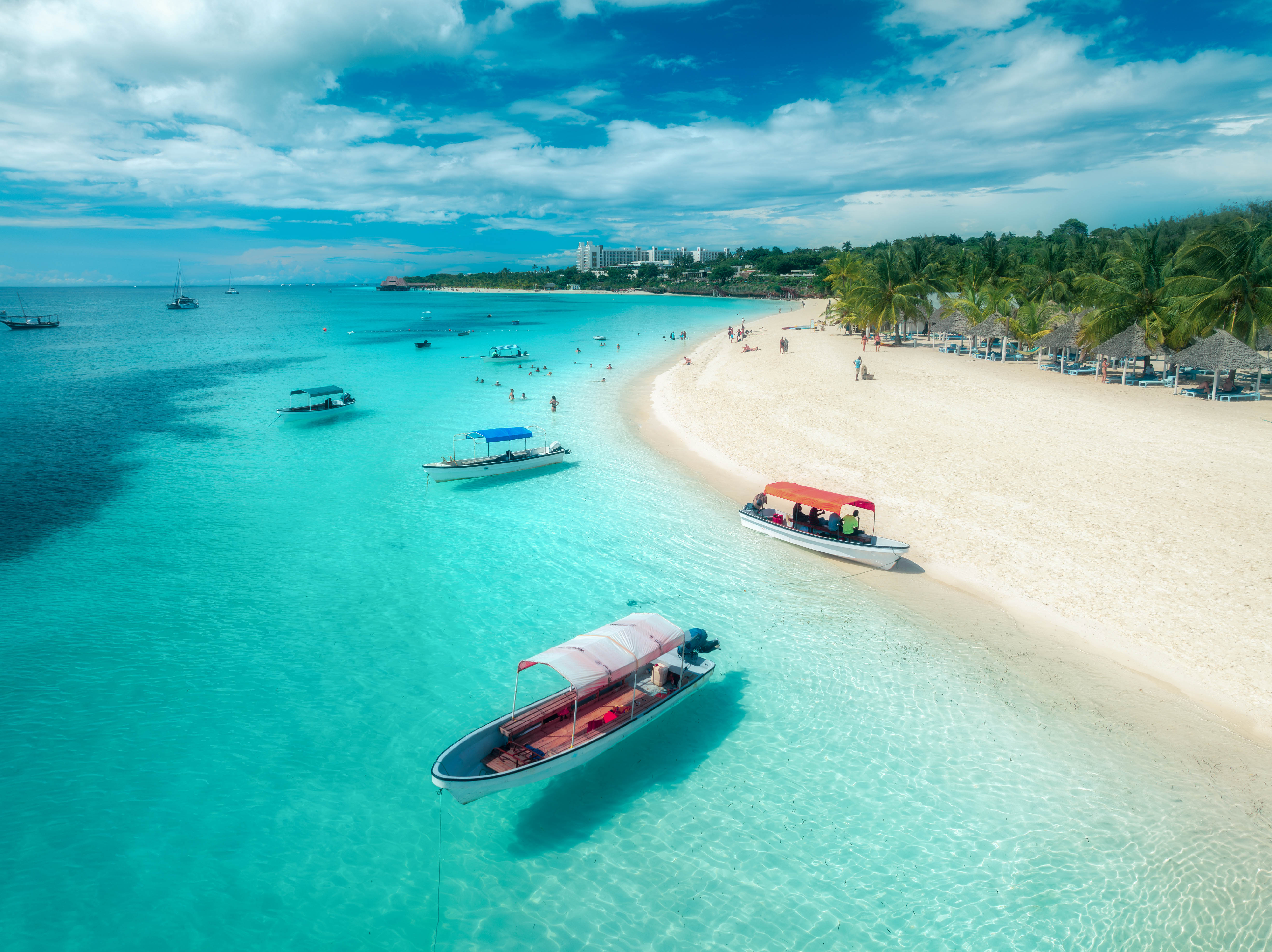 Urlop w Tunezii - Ubezpieczenie turystyczne Łódki i turyści relaksujący się na plaży Zanzibaru