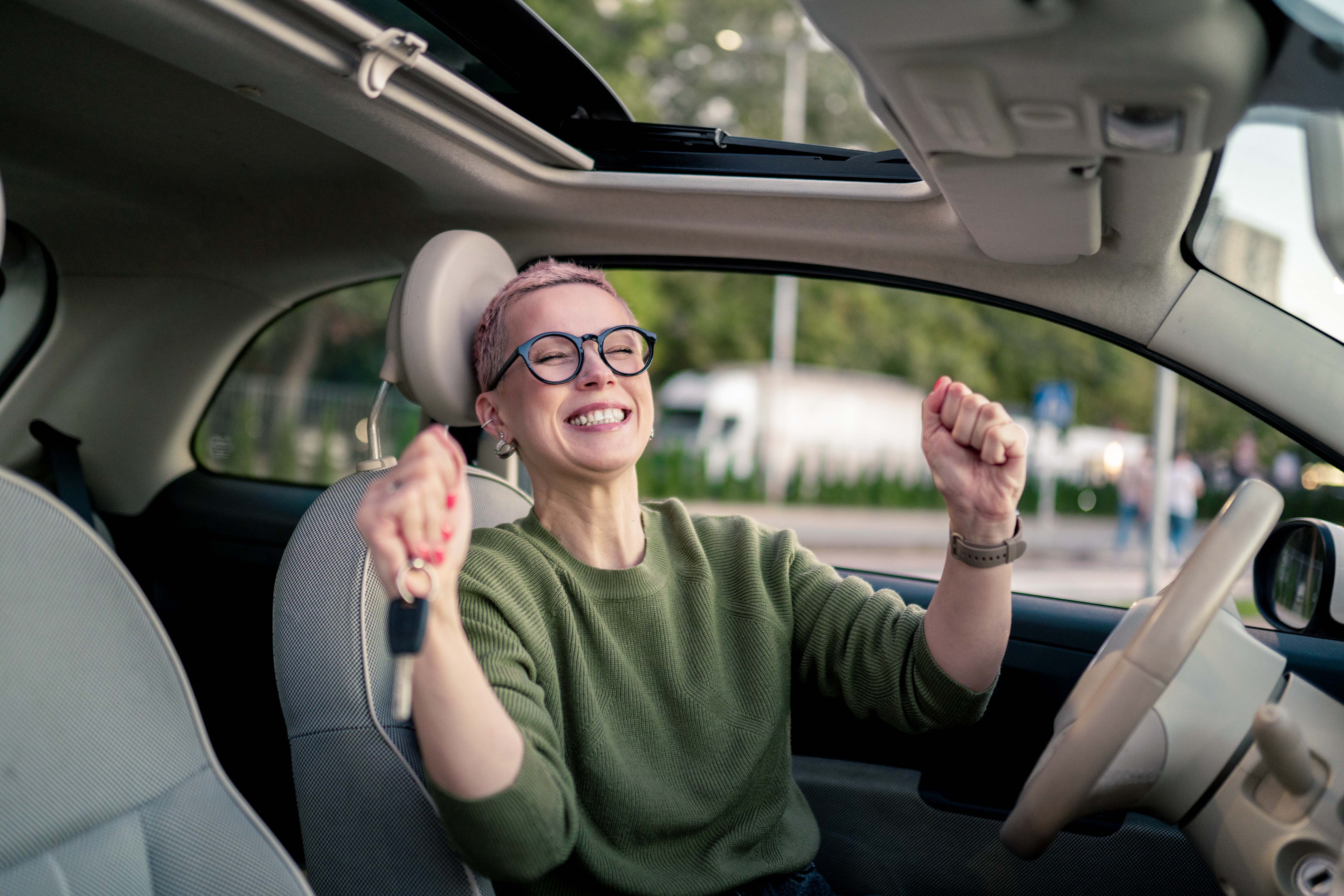 Kobieta cieszy się odebranym prawem jazdy po zdanym egzaminie i wsiada pierwszy raz za kółko swojego auta