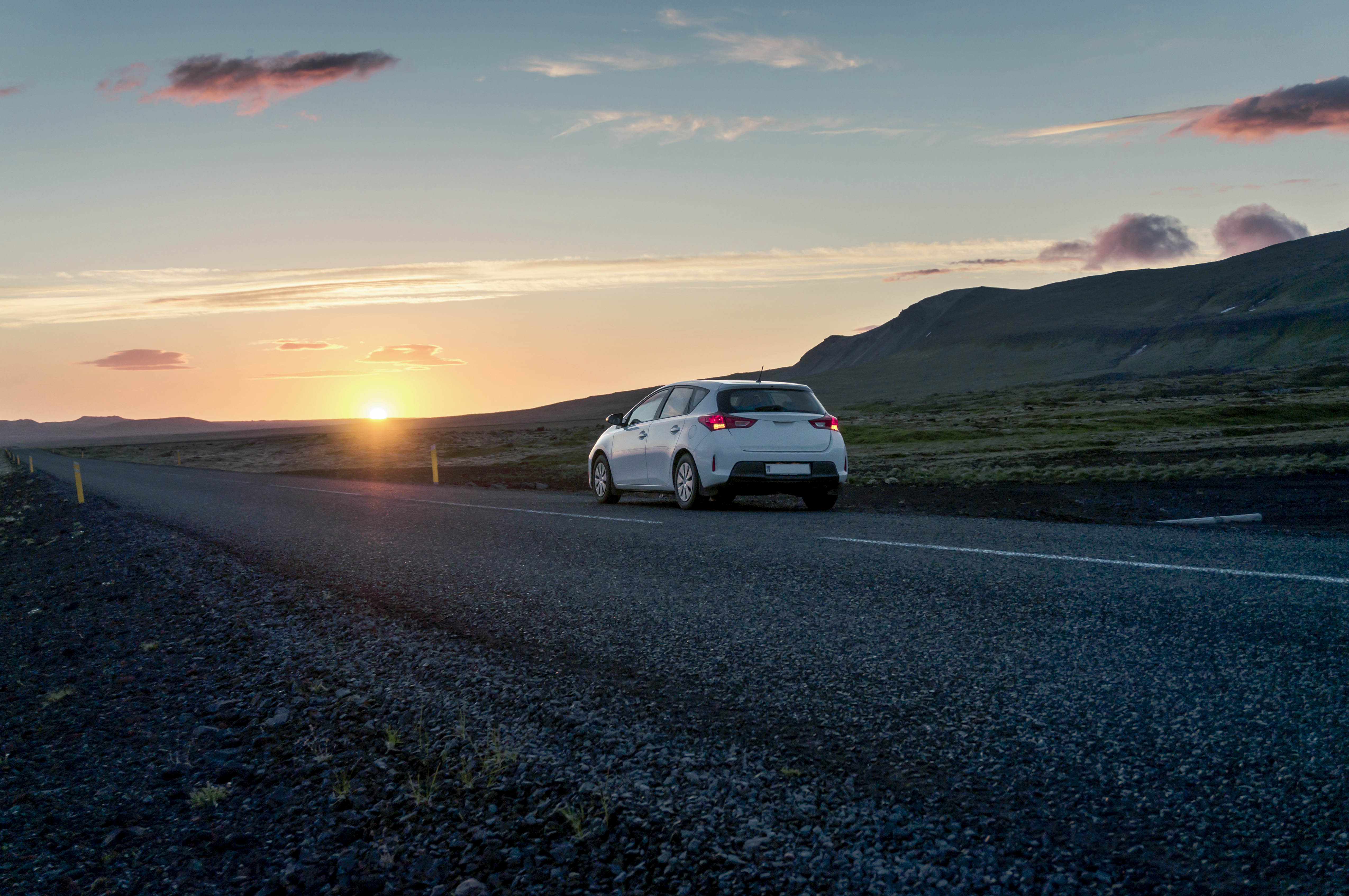 Samochód hatchack jedzie drogą o zachodzie słońca.